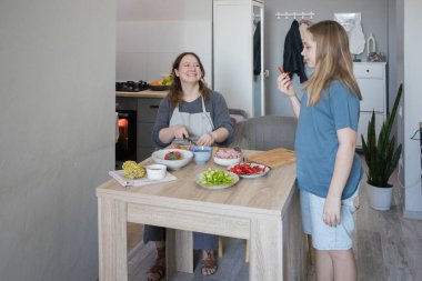 Evcil mutfakta sebze yiyen ve annesiyle sohbet eden tatlı bir kız çocuğu.