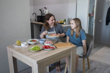 Mutlu kız ve annesi birlikte ev mutfağında yemek pişiriyorlar, aile hayatı portresi yapıyorlar.