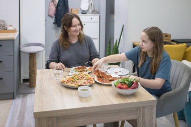 Anne ve kızı evde pizza yiyorlar.