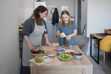 Genç kız ve annesi birlikte ev mutfağında yemek pişiriyorlar, aile hayatı portresi yapıyorlar.