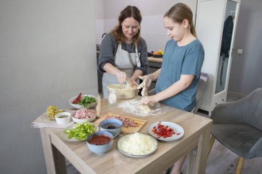 Gülümseyen aile içeride. Anne ve kızı birlikte mutfakta pizza pişiriyorlar.