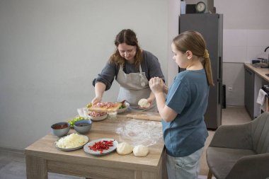 Ev pizzası hazırlığı. Çocuk kız ve anne pizza için hamur hazırlıyor ve evde yemek pişirirken gülümsüyor.