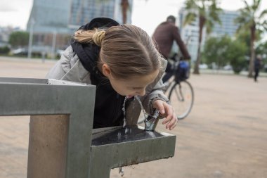 Genç kız çeşmeden su içiyor. Ferahlama ve susuzluk kavramı, kız susuzluğunu gidermek için güne ara veriyor.