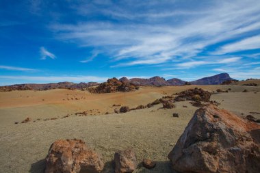 Mavi gökyüzü, bulutlar ve çöl tepeleriyle doğa manzarası.