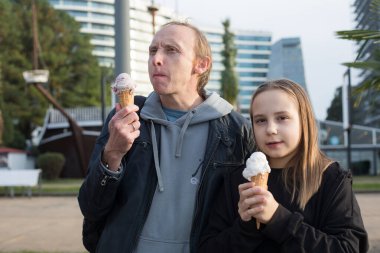 Küçük kız ve babası dışarıda yürüyüp dondurma yiyorlar. Mutlu aile, çocukluk ve hafta sonu konsepti.