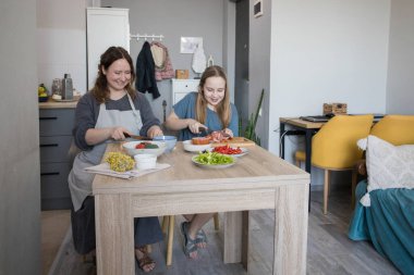 Neşeli kız ve annesi birlikte ev mutfağında yemek pişiriyorlar, aile hayatı portresi yapıyorlar..