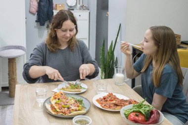 Anne ve kızı evde akşam yemeği için ev yapımı pizza yiyorlar..