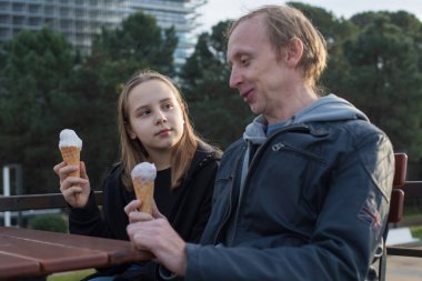 Mutlu baba-kız dondurma yiyorlar. Şehir merkezindeki kafede oturuyorlar. Mutlu aile, çocukluk, boş zaman aktivitesi ve hafta sonu konsepti.