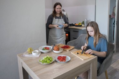 Sağlıklı kız ve annesi birlikte ev mutfağında yemek pişiriyorlar, aile hayatı portresi yapıyorlar..