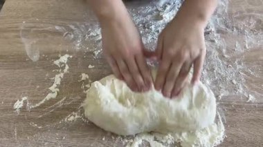 Kadın bir aşçının elleri, beyaz buğday unuyla ahşap bir masada hamur yoğurur..