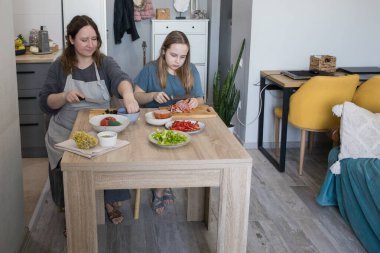 Yoğunlaşmış kız ve annesi birlikte ev mutfağında yemek pişiriyorlar, aile hayatı portresi yapıyorlar.