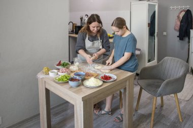 Çalışkan çocuk kız ve anne pizza için hamur hazırlıyor ve evde yemek pişirirken gülümsüyor. Aile bir arada.