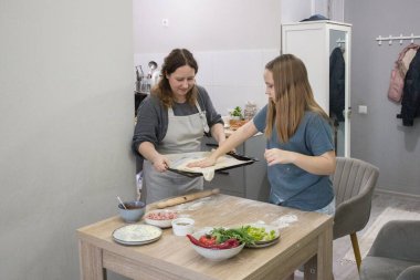 Sevimli kız, annesiyle mutfakta pizza pişiriyor.