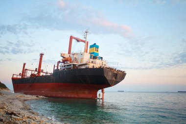 Gün batımında gökyüzünün altında beyaz bulutlarla karaya oturmuş bir gemi.