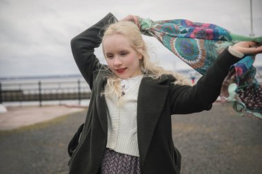 Sarışın, güzel bir kadın. Açık havada yürüyor, portresi var.