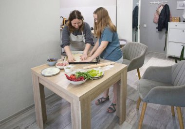 Gülümseyen kız annesiyle mutfakta pizza pişiriyor.