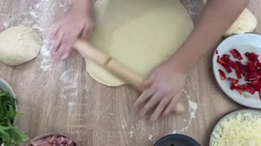 Kadın bir aşçının elleri, beyaz buğday unuyla ahşap bir masada hamur yoğurur..