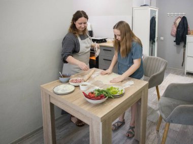 Güzel kız annesiyle mutfakta pizza pişiriyor.