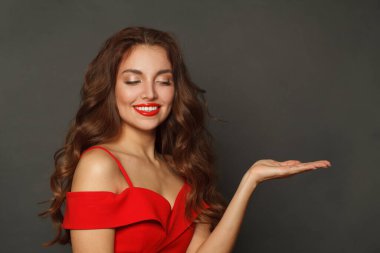 Güzel model bir kadın boş avuç içini tutuyor ve siyah arka planda gülümsüyor. 