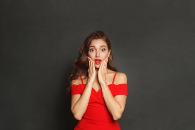 Kıvırcık saçlı, makyajlı, yüzü siyah arka planda olan şaşırmış bir kadın.