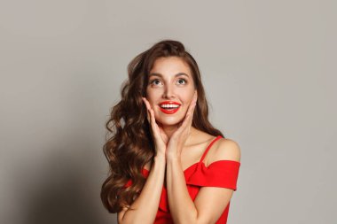 Kıvırcık saçlı, makyajlı, yüzü siyah arka planda olan hoş, şaşkın bir kadın.