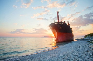 Denizde kızıl bir gemi. Gün batımı altında bulutlar ve güneş ışığı altında.