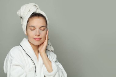 Nemlendirici, gençleştirici beyaz kumaş maskeli, beyaz arka planda kameraya gülümseyen genç bir kadın.