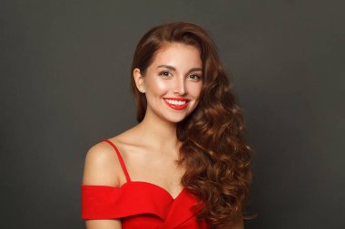 Esmer makyajlı, kahverengi kıvırcık saçlı, siyah arka planda kırmızı dudaklı esmer kadının stüdyo portresi. 