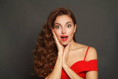 Şok olmuş, kıvırcık saçlı, makyajlı, yüzü siyah arka planda olan bir kadın.