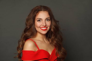 Moda makyajlı, kahverengi kıvırcık saçlı, dalgalı saçlı ve siyah arka planda kırmızı dudaklı mutlu esmer kadın. 