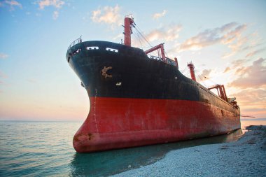 Kızıl kargo gemisi bulutlarla birlikte gün batımında sığ bir denizde mahsur kaldı.