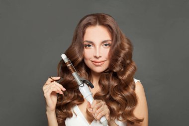 Uzun dalgalı saç stili olan çekici bir kadın saç maşası, maşa, iç mekan portresi kullanıyor. Kuaför aletleri ve saç şekillendirme konsepti