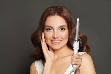 Uzun dalgalı saç stili, saç maşası maşası, iç mekan portresi kullanan bir kadının yakın plan portresi. Kuaför aletleri.