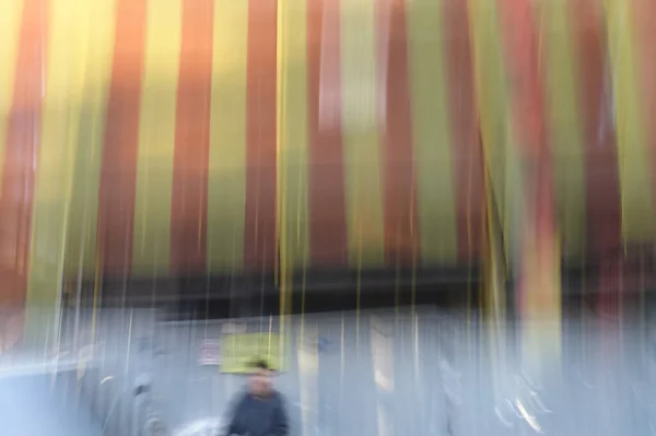 建築標識や縞模様の破片ネットドレープの建物の下で段ボールフェンスの横に人間の姿を赤らめる 意図的なカメラの動き抽象的な通りの写真 — ストック写真