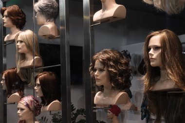 Kadınlar için peruklu oyuncak bebek kafaları. Geceleri pencere görüntüsü.