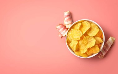 Bir kase çıtır patates cipsi ya da pembe arka planda domuz pastırması aromalı cips, üst manzara, metin için boş alan