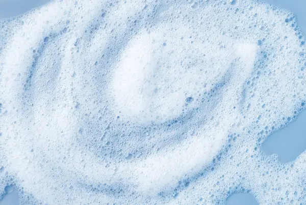 White skincare cleansing foam bubbles on light blue background. Soap, shampoo or shower gel foam texture, close-up, top view