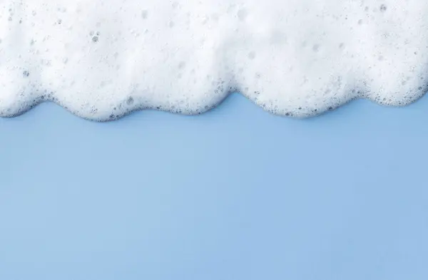 White skincare cleansing foam bubbles on light blue background. Soap, shampoo or shower gel foam texture, close-up, top view