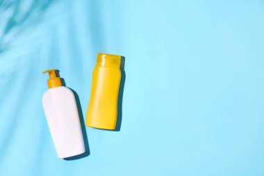 Açık mavi arka planda sarı ve beyaz güneş kremi şişeleri, üst manzara. Güneş koruma ürünleri. Boş şişe maketi