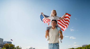 Vatansever bayram. Mutlu aile, baba ve kız çocuğu açık havada Amerikan bayrağı taşıyor. ABD 4 Temmuz 'u kutladı.