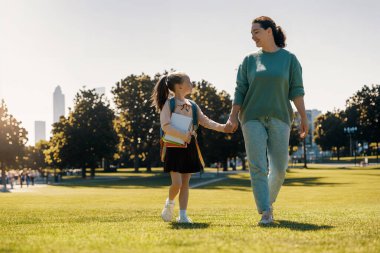 İlkokulun ebeveyni ve öğrencisi el ele gidiyor. Sırt çantalı kadın ve kız. Dersler başlıyor..