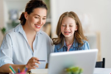 Mutlu çocuk ve yetişkin masada oturuyor. Ödev yapan ya da online eğitim alan kız.