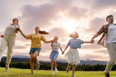 Gün batımında mutlu bir aile. Baba, anne ve çocuklar koşuyor, eğleniyorlar ve yaz akşamının tadını çıkarıyorlar.. 