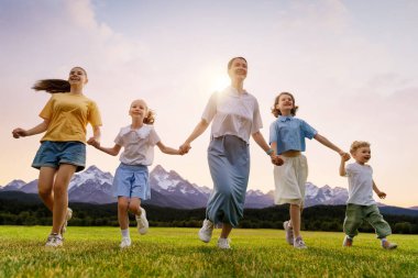 Gün batımında mutlu bir aile. Anne ve çocuklar koşuyorlar, eğleniyorlar ve yaz akşamının tadını çıkarıyorlar.. 