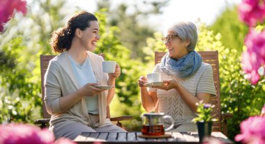 Mutlu genç kadın ve annesi yaz sabahı çay içiyorlar. Aile bahçede fincanlarla oturuyor ve sohbetin tadını çıkarıyor..