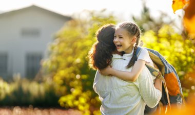 Ebeveyn ve çocuk okula gidiyor. Sırt çantalı kadın ve kız. Dersler başlıyor..