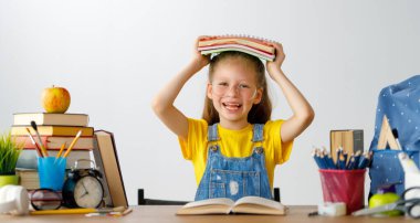 Okula dönün! Mutlu, sevimli, çalışkan çocuk kapalı bir masada oturuyor. Çocuk derste ya da derste öğreniyor.