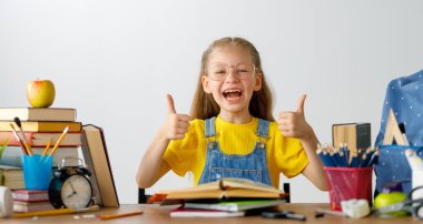 Okula dönün! Mutlu, sevimli, çalışkan çocuk kapalı bir masada oturuyor. Çocuk derste ya da derste öğreniyor.