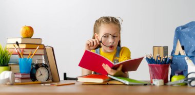 Okula dönün! Mutlu, sevimli, çalışkan çocuk kapalı bir masada oturuyor. Çocuk derste ya da derste öğreniyor.