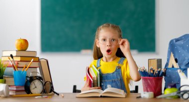 Okula dönün! Mutlu, sevimli, çalışkan çocuk kapalı bir masada oturuyor. Çocuk sınıfta tahtada öğreniyor..